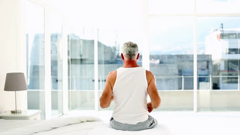 Mature-man-yawning-and-stretching-sitting-on-bed