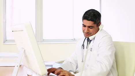 Doctor-working-at-his-computer-and-talking-on-phone