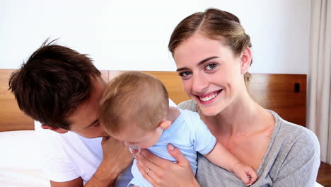 Happy-parents-sitting-on-bed-with-their-baby-son