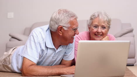 Senior-couple-lying-on-floor-using-laptop