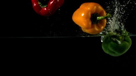 Three-peppers-falling-in-water-on-black-background