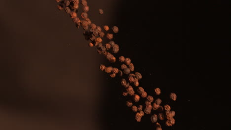 Pepper-corns-falling-against-black-background