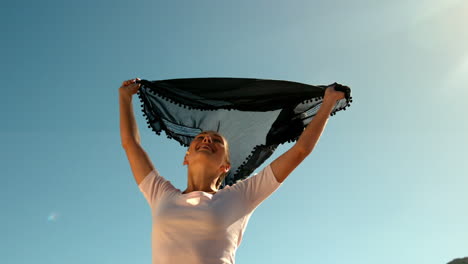 Happy-woman-holding-black-scarf-above-head-on-sunny-day