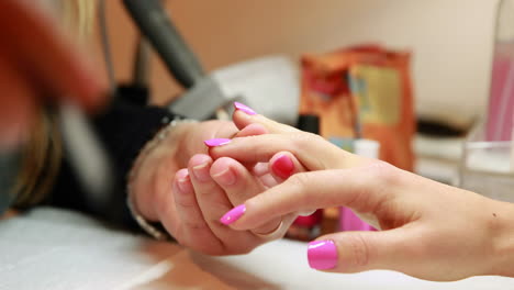 Nail-technician-painting-top-coat-onto-customers-pink-nails