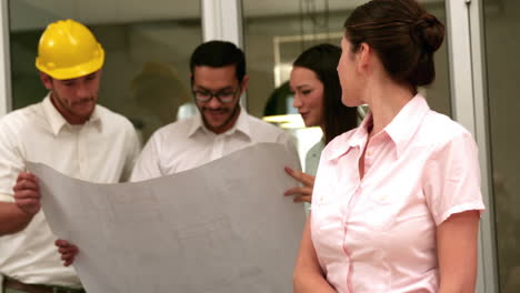 Equipo-De-Arquitectos-Revisando-Planos-Con-Uno-Sonriendo-A-La-Cámara.