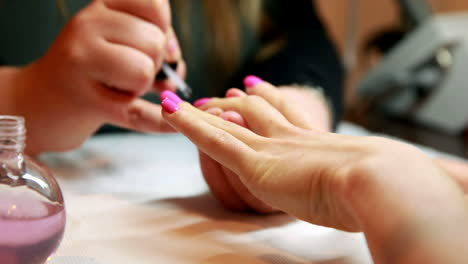 Nail-technician-painting-top-coat-onto-customers-pink-nails