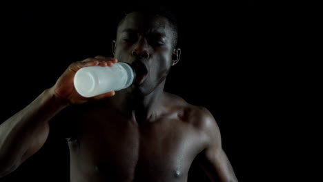 Shirtless-man-jogging-and-drinking-water-against-black-background