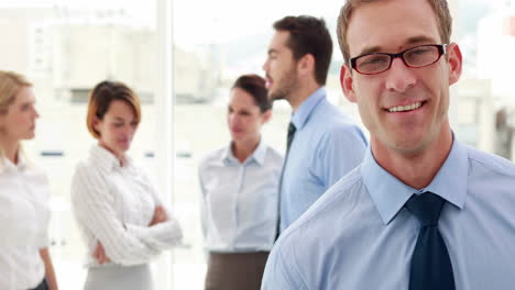 Businessman-smiling-at-camera-with-colleagues-behind-him