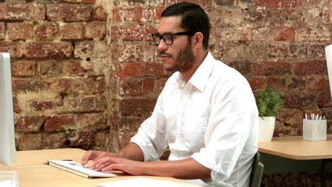 Casual-businessman-working-at-his-desk-smiling-at-camera