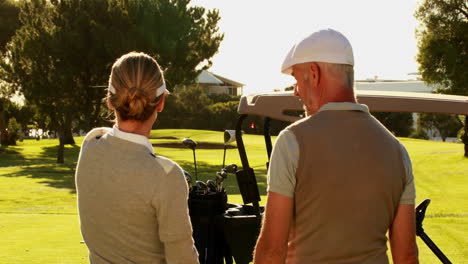 Pareja-De-Pie-En-El-Campo-De-Golf-Mirando-A-Su-Alrededor