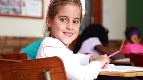 Little-girl-colouring-in-the-classroom-and-smiling-at-camera