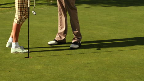 Pareja-De-Pie-En-El-Putting-Green-Del-Campo-De-Golf