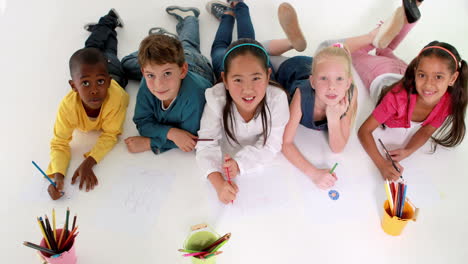 Cute-children-lying-on-floor-drawing-on-paper-and-waving-at-camera