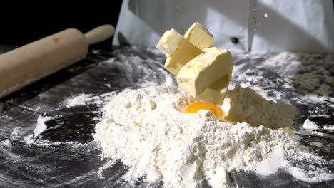 Chef-adding-butter-to-raw-egg-and-flour-on-black-surface