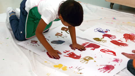 Cute-little-boys-painting-with-hands-lying-on-paper-in-classroom