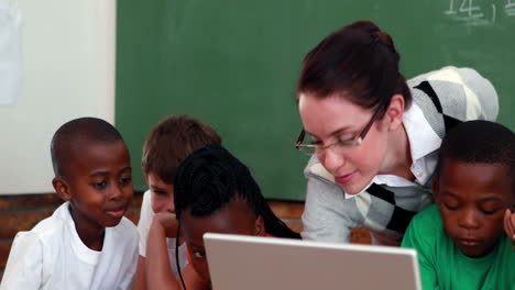 Pupils-and-teacher-looking-at-laptop-in-classroom