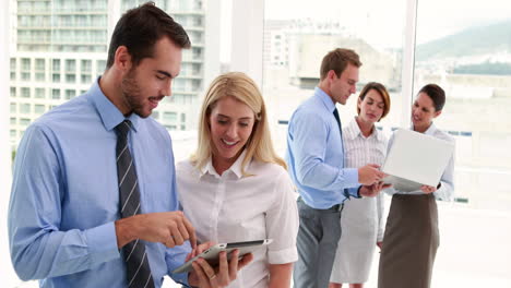 Business-team-using-tablet-and-smiling-at-camera-together