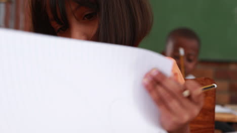 Little-girl-turning-pages-in-classroom-at-her-desk