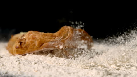 Pastry-snack-falling-on-flour-on-black-background