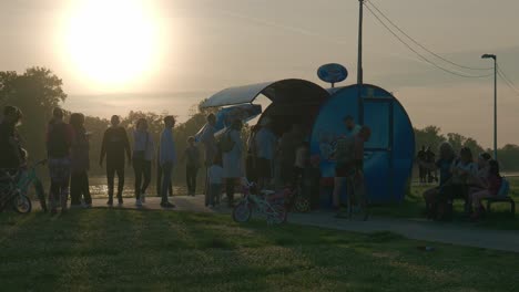 Group-of-people-gathering-at-a-lakeside-kiosk-during-sunset-at-Jarun-Lake,-Zagreb-Croatia