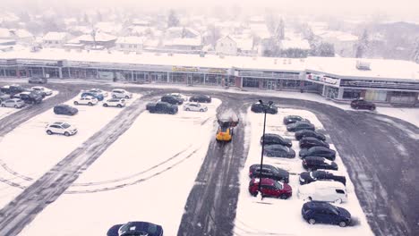 Winter-parking-lot-of-a-strip-mall-as-a-snowplough-bulldozer-clears-the-snow-and-ice-from-the-tarmac