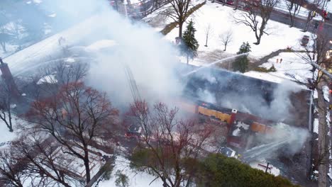 Aerial-drone-shot-descending-onto-a-smoldering-abandoned-kindergarten-school-after-a-fire-as-firefighters-continue-to-extinguish-the-blaze