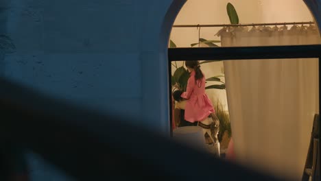 Maniquí-Vestido-Con-Un-Traje-Rosa-Visto-A-Través-De-Una-Ventana,-Colocado-Sobre-Un-Caballito-En-El-Interior