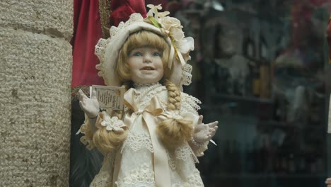 Close-up-of-a-vintage-doll-in-an-elaborate-lace-dress,-displayed-in-a-shop-window-in-Venice,-Italy