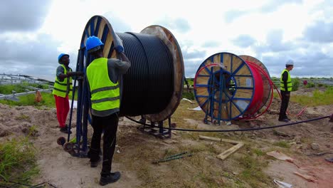 African-technicians-and-engineers-unreeling,-laying-electrical-power-cables-at-renewable-energy-solar-farm---static-wide-shot