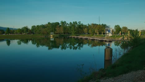 Reflections-of-trees-and-a-modern-structure-in-a-calm-lake-with-a-clear-sky-at-Jarun-Lake,-Zagreb