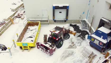 Aerial-drone-shot-looking-down-on-a-tractor-ploughing-snow-and-ice-from-the-delivery-bay-of-a-business