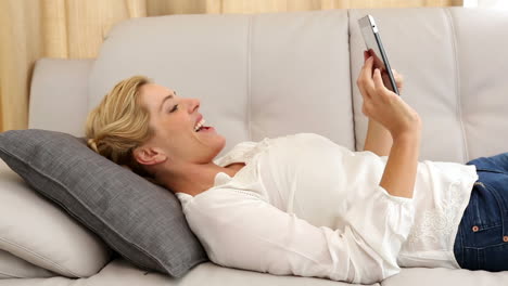 Glückliche-Blondine-Mit-TabletPC-Auf-Der-Couch