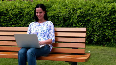 Woman-sitting-on-park-bench-using-laptop
