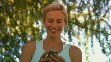 Fit-blonde-sending-a-text-in-the-park