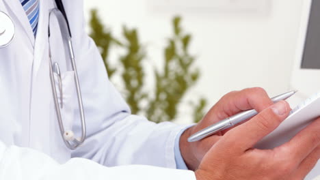 Doctor-writing-on-clipboard-at-his-desk