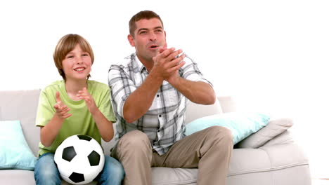 In-slow-motion-happy-father-and-son-with-football-watching-tv