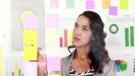 Smiling-businesswoman-looking-post-its-on-the-wall