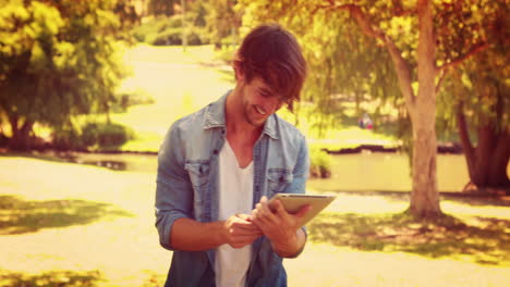 Handsome-man-using-tablet-and-laughing-in-the-park