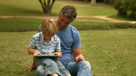 Glücklicher-Vater-Mit-Seinem-Sohn-Mit-Tablet-Im-Park