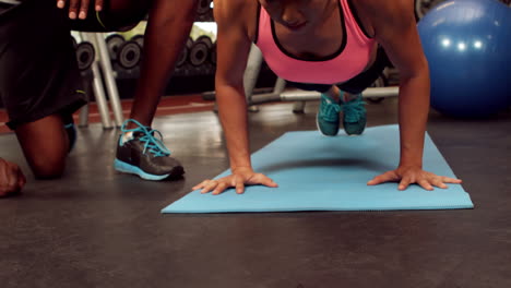 Entrenador-Masculino-Ayudando-A-Una-Mujer-Con-Flexiones