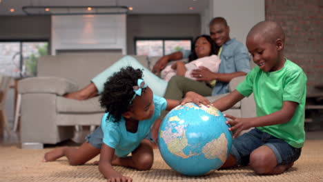 Siblings-looking-at-globe-on-the-floor-while-parents-watch