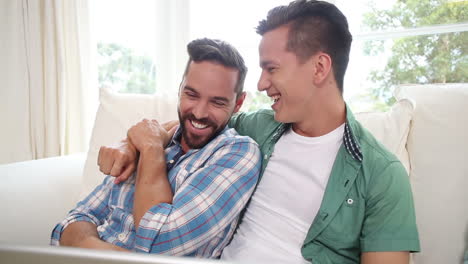 Pareja-Gay-Relajándose-En-El-Sofá-Usando-Una-Computadora-Portátil