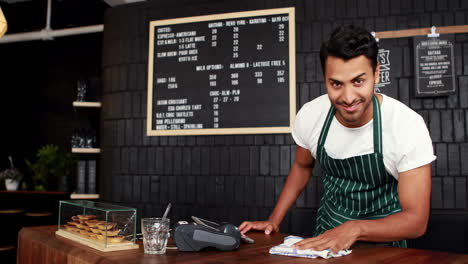 Smiling-handsome-waiter-cleaning-counter