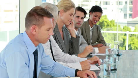 Business-team-taking-notes-during-conference-while-colleague-having-a-phone-call