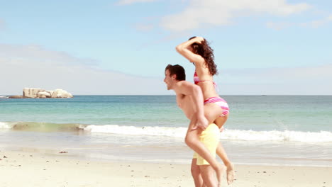 Man-giving-his-girlfriend-a-piggy-back-at-the-beach