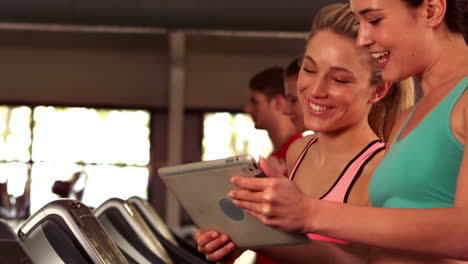 Fit-women-looking-a-tablet-while-fit-people-running-on-treadmills