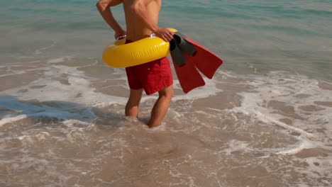 Man-wearing-flippers-and-rubber-ring-walking-in-the-sea