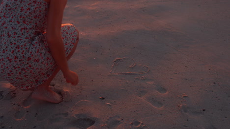 Woman-drawing-heart-on-sand-