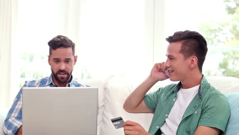 Pareja-Gay-Relajándose-En-El-Sofá-Usando-Una-Computadora-Portátil