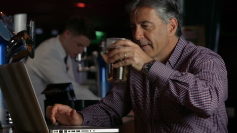 Man-having-a-pint-at--the-bar-using-laptop